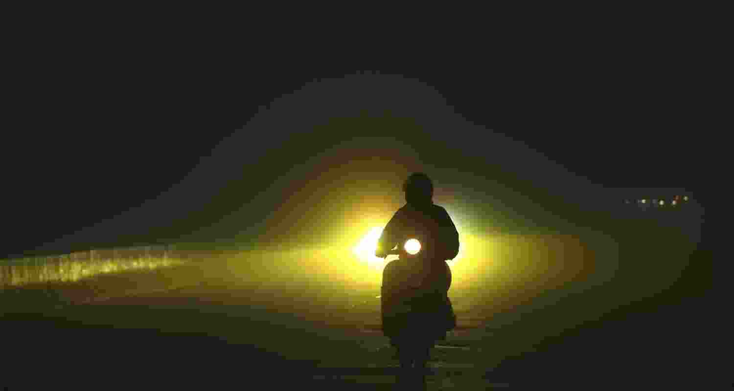 A scooter rider navigates a road amid low visibility on a foggy winter morning, in Jammu. 