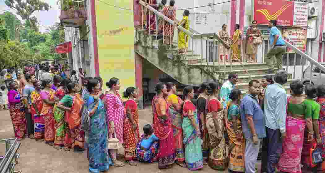 People stand in queue outside a Post Office to complete the verification process for the ‘Annapurna Yojana‘ financial assistance scheme for women, in Balurghat, West Bengal.