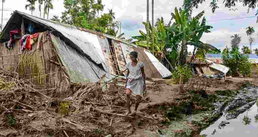 A woman walks past a damaged house affected by the flood in Assam.