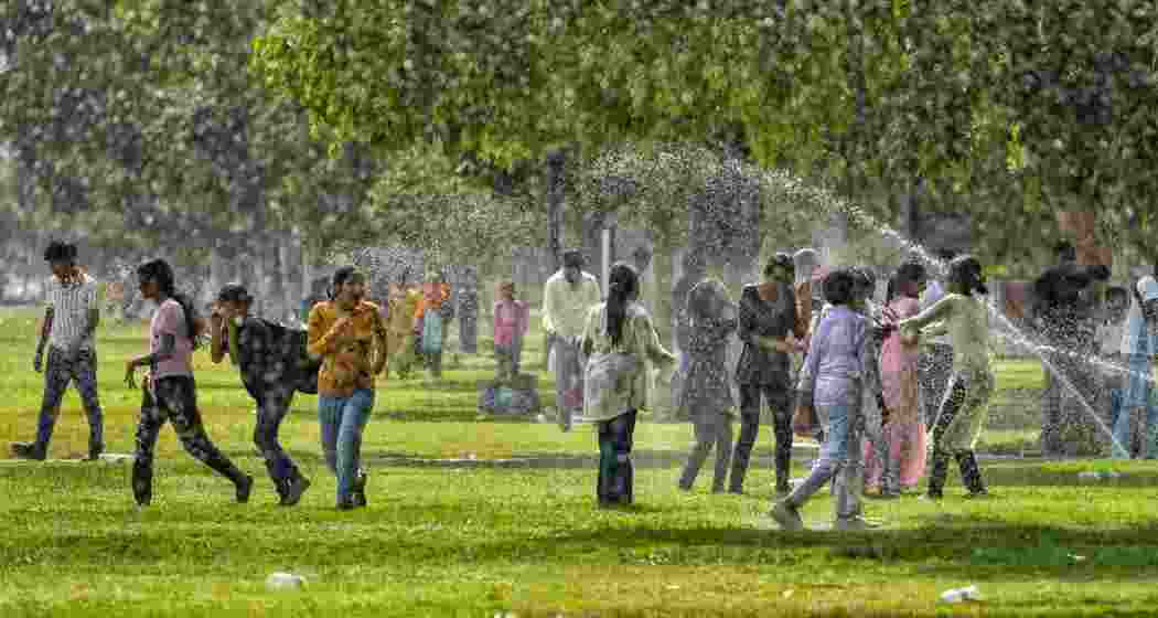 Visitors get drenched as they stand near sprinklers for respite from the scorching heat, at the lawns near Kartavya Path in New Delhi, Monday.