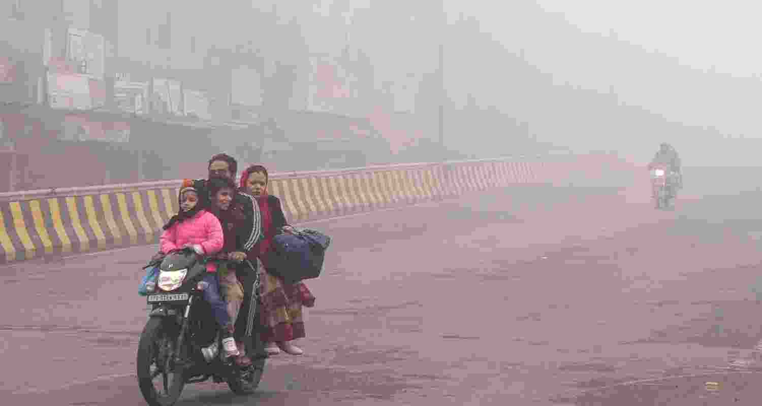 A family rides a motorcycle amid dense fog during a cold winter morning, in Amritsar. 