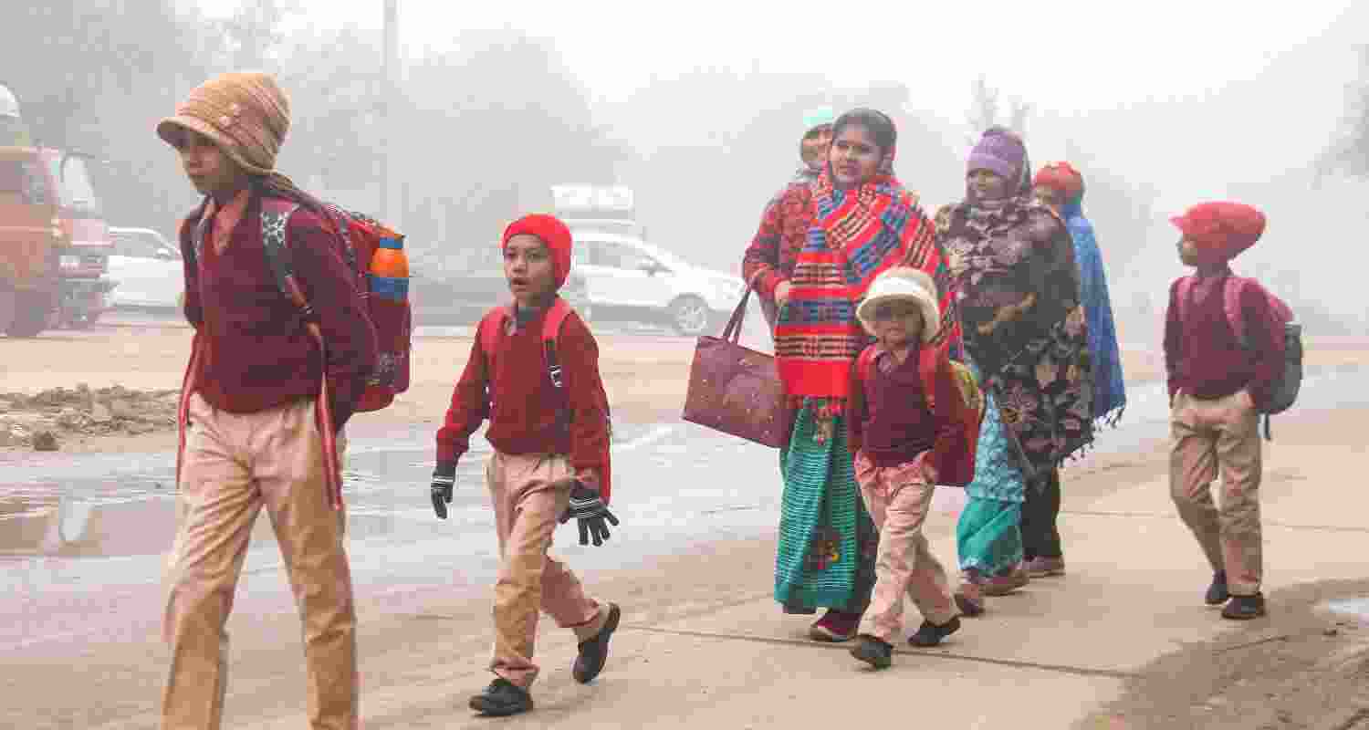 Students wearing warm clothes along with their guardians walk to their school during a foggy and cold winter morning, in Gurugram. 