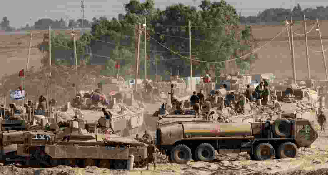 Israeli soldiers organize military equipment while standing on armored personnel carriers near the border with the Gaza Strip.