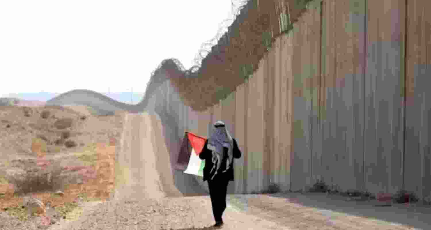A man walks with a Palestinian flag in front of the Israeli separation barrier near Hebron in the West Bank in 2022.