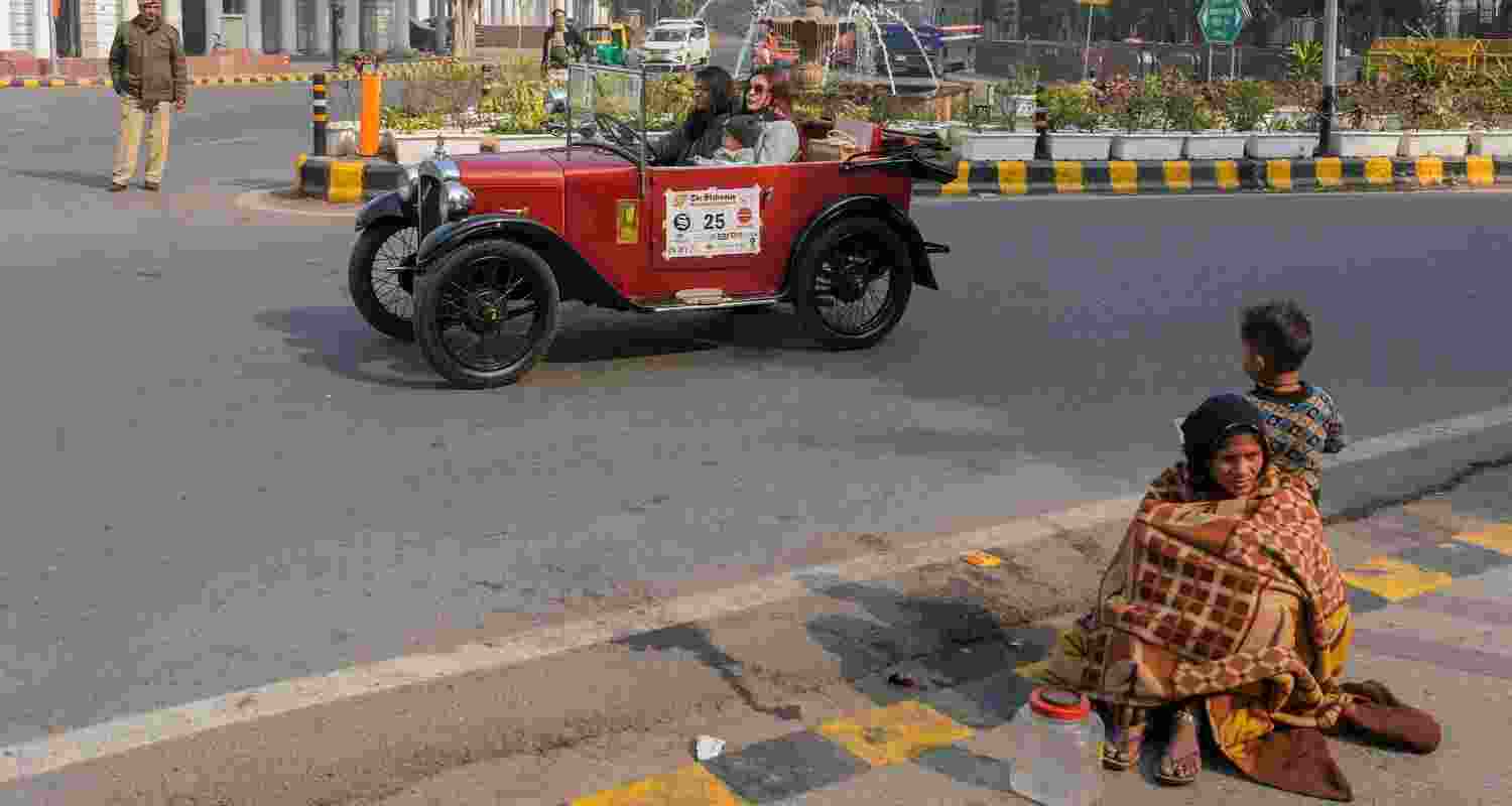 Two worlds apart: Two women ride their vintage car, while a homeless woman sits at the curb with a child, at the 57th edition of the Statesman Vintage & Classic Car Rally, at Connaught Place, in New Delhi.
