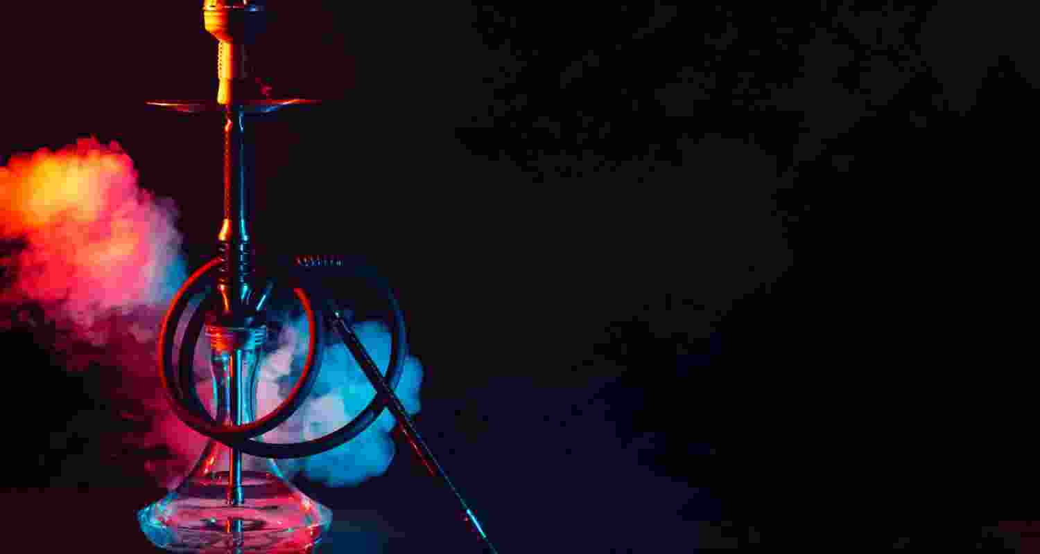 Photo glass hookah shisha with a metal bowl on the table on a black background with smoke and colored neon lighting.