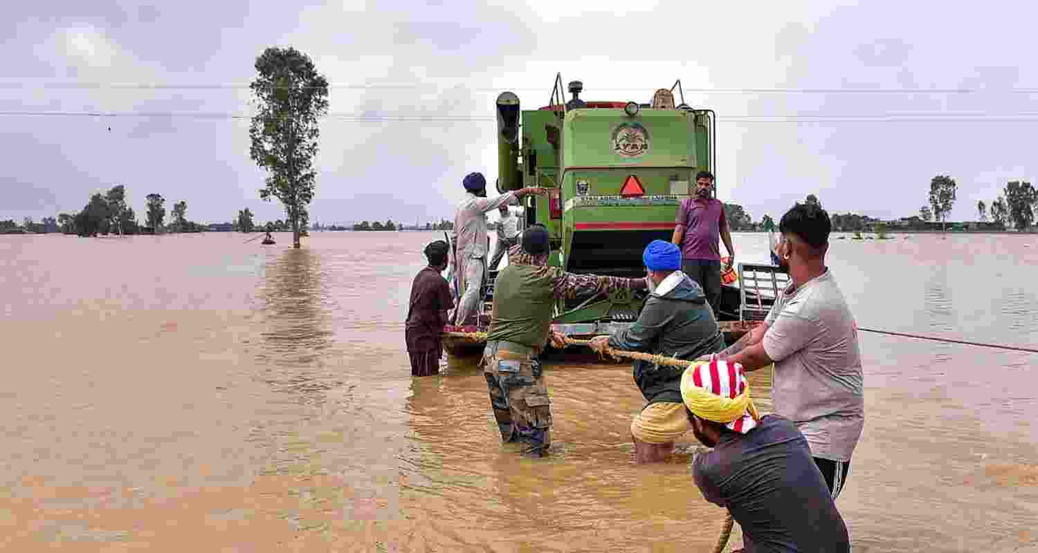 Security personnel and locals pull a boat loaded with an agricultural machine, through a flooded area, in Kapurthala, Punjab.