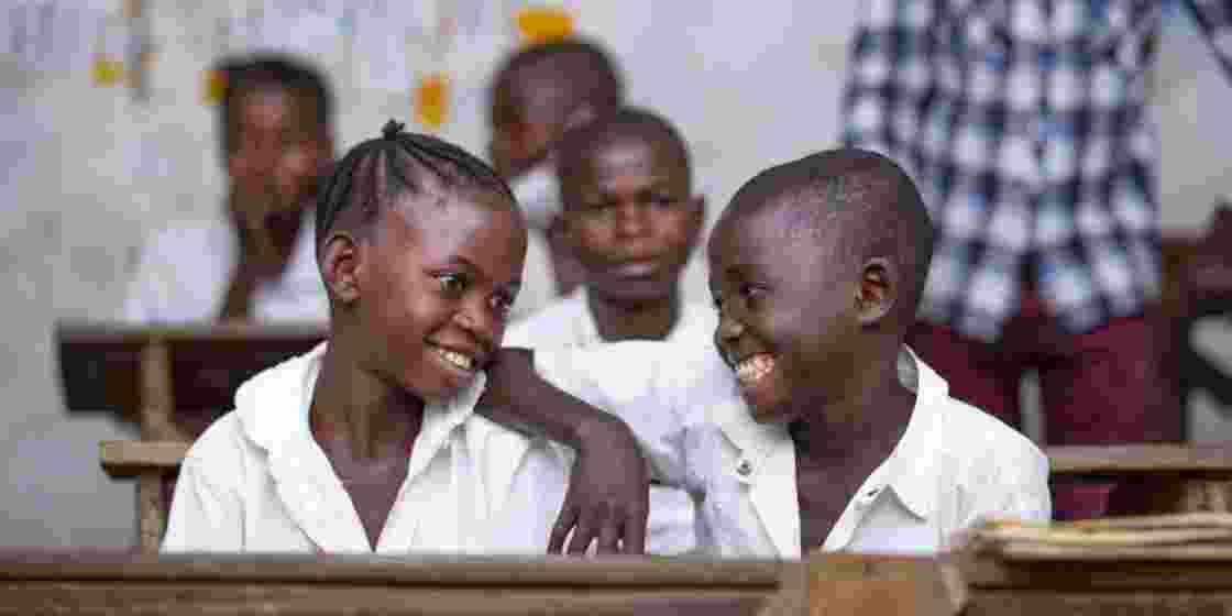 A young schoolgirl and schoolboy share a joyful moment in class.