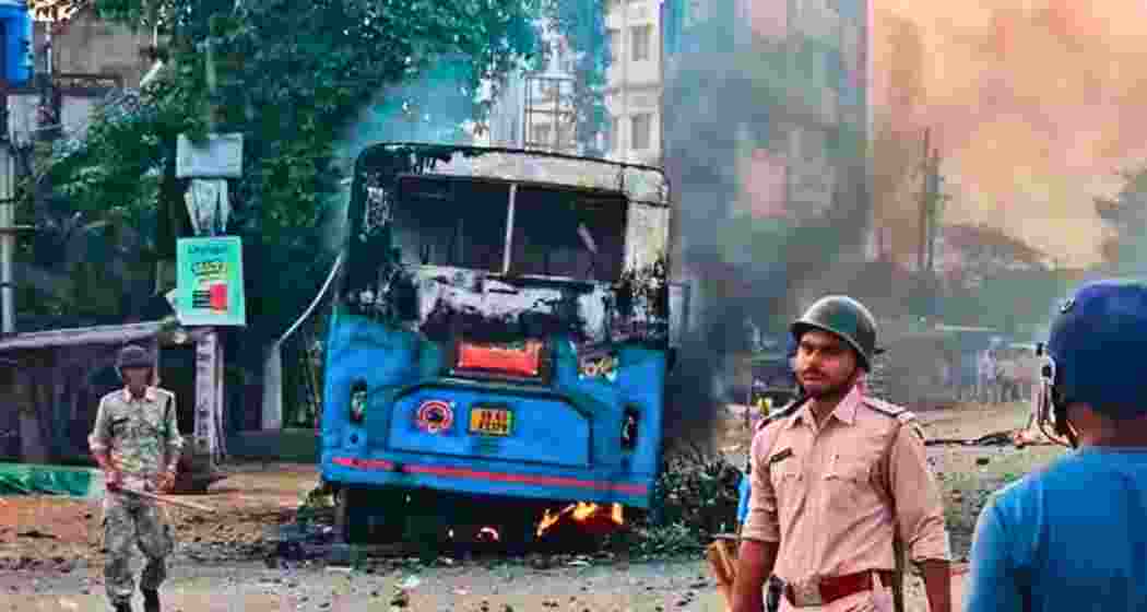 Security personnel stand near a torched vehicle during a protest against Waqf (Amendment) Act, in Murshidabad district.