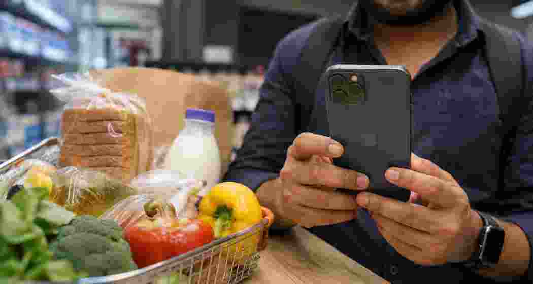 A customer uses a premium smartphone while shopping for groceries, symbolising India’s shift in consumer spending from essentials to digital services, gadgets and lifestyle experiences. (Representational Image) A customer uses a premium smartphone while shopping for groceries, symbolising India’s shift in consumer spending from essentials to digital services, gadgets and lifestyle experiences. (Representational Image)